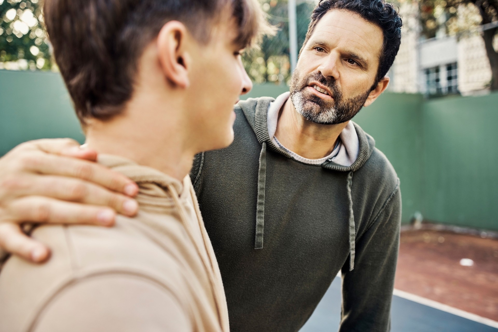 Father and son walking after playing a game of basketball. Young man and teenage boy having talking and chatting while staying fit, active