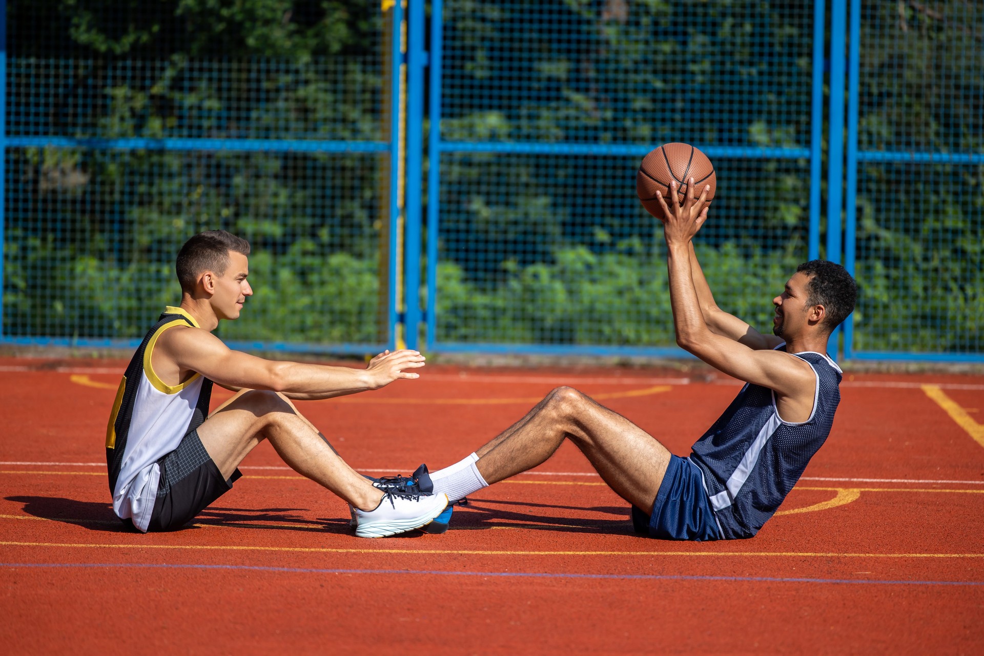 Multicultural men friends having training with ball while sitting on floor on court
